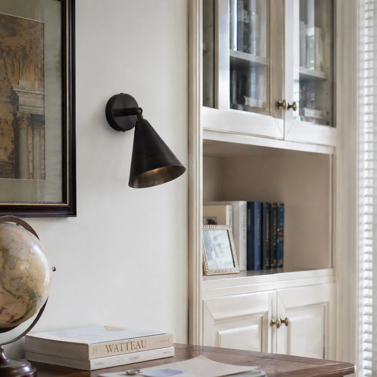 Matte black brass wall light above books and a desk corner