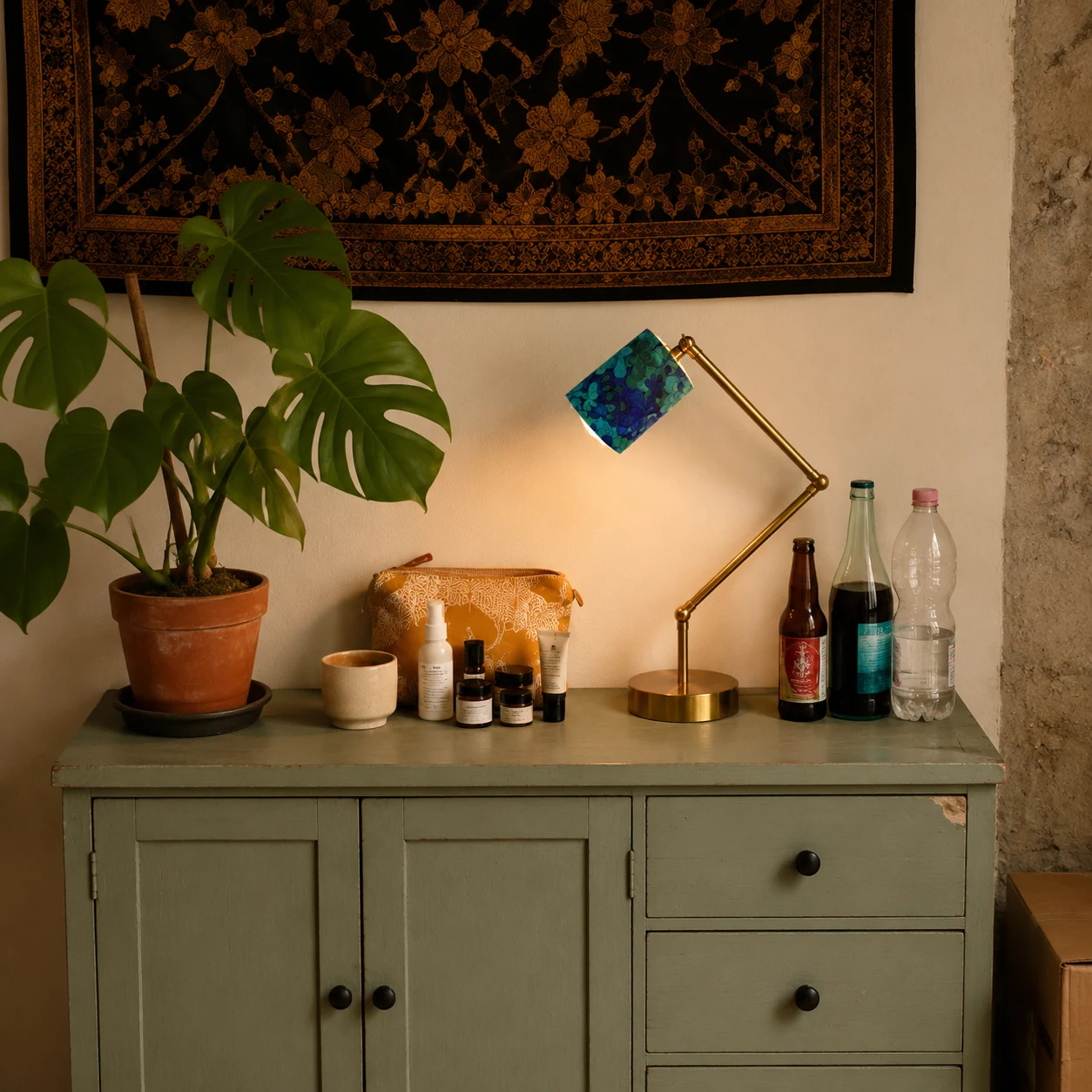 Blue green floral table lamp lit on a console with plants and decor