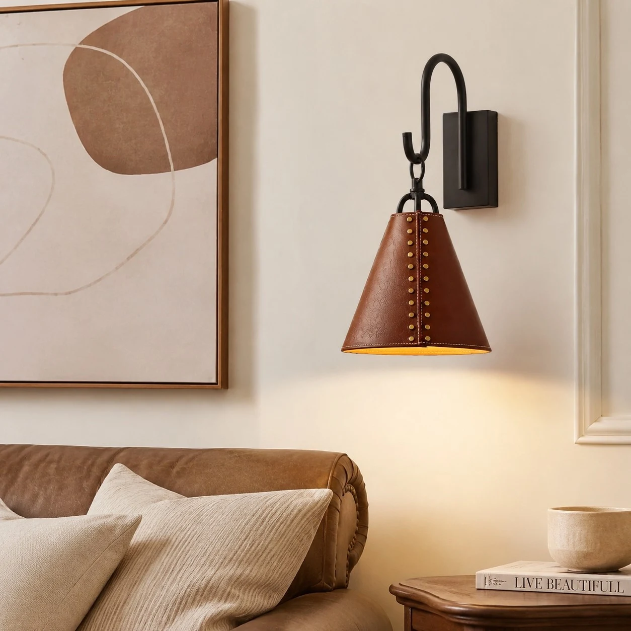 Leather cone wall sconce casting warm light beside a bed and framed wall art