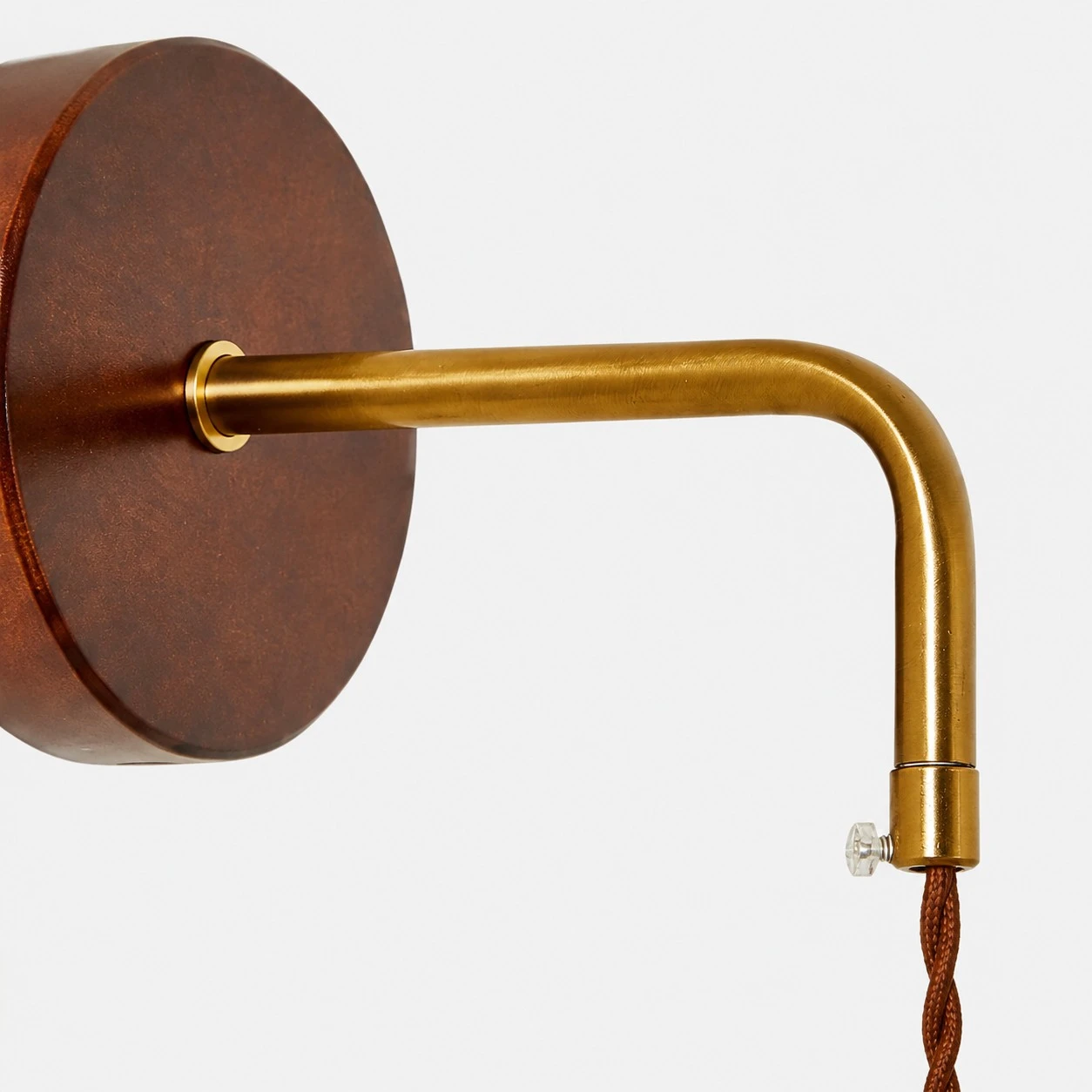 Close view of the round wooden wall plate and brass arm connection on the bedside wall lamp