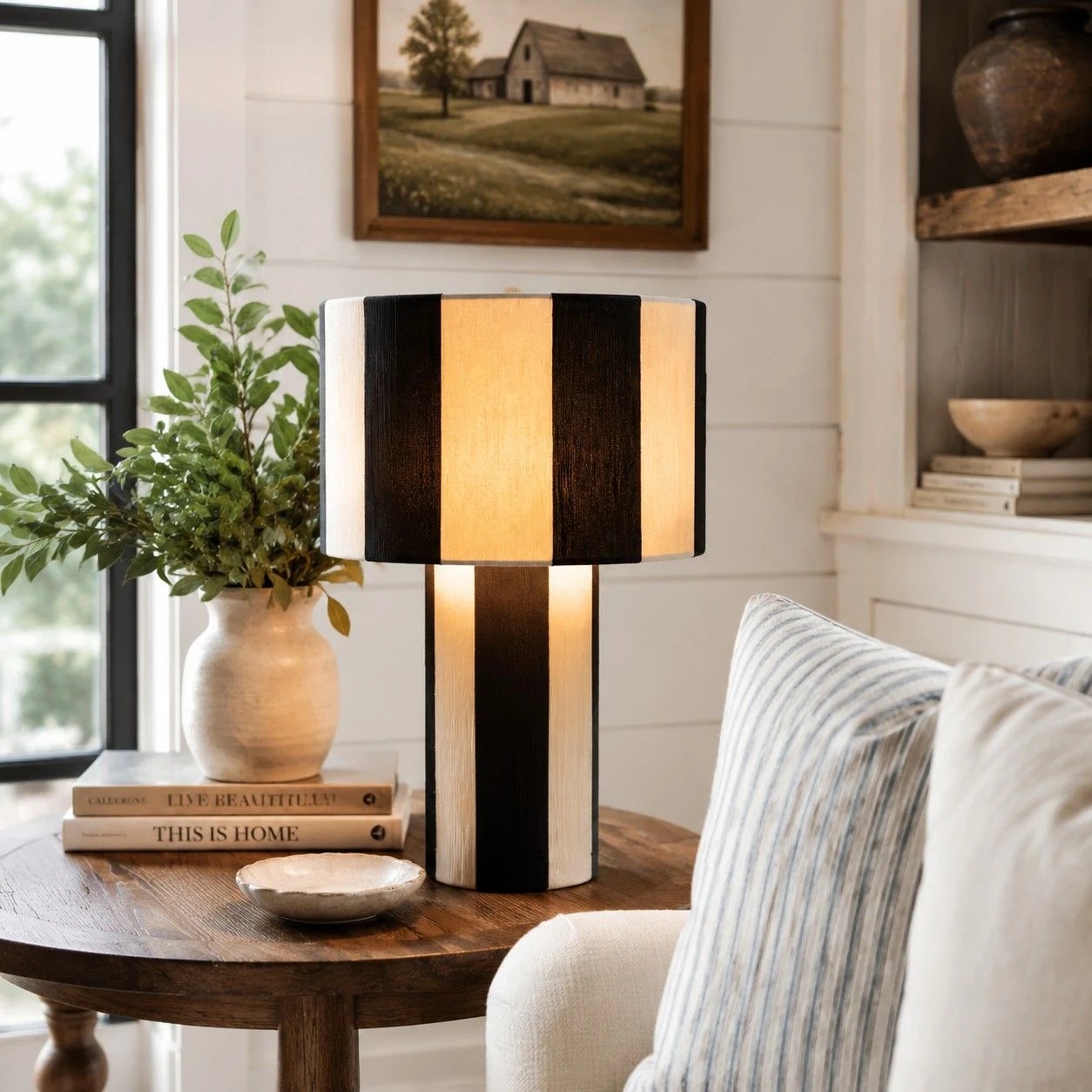 Black and white striped woven table lamp lit on a wood side table